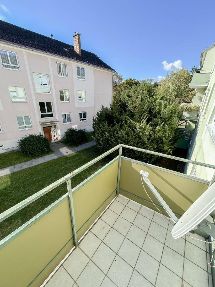 Balkon mit Fliesenboden und Blick auf die grüne Umgebung und das gegenüberliegende Gebäude.