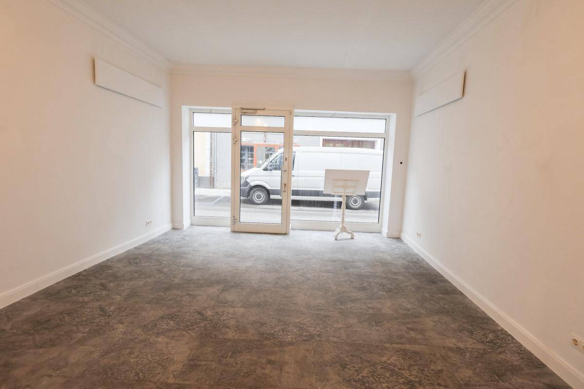 Heller Geschäftsraum mit großen Schaufenstern zur Straße und modernem Bodenbelag, ideal für Einzelhandel oder Büro.