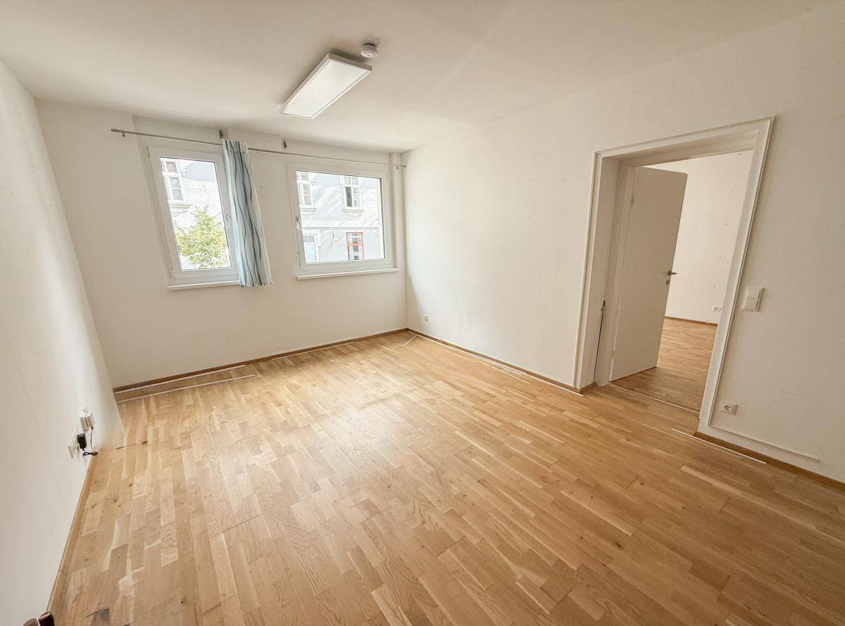 Leeres Zimmer mit Parkettboden und zwei Fenstern, bereit zur individuellen Gestaltung.