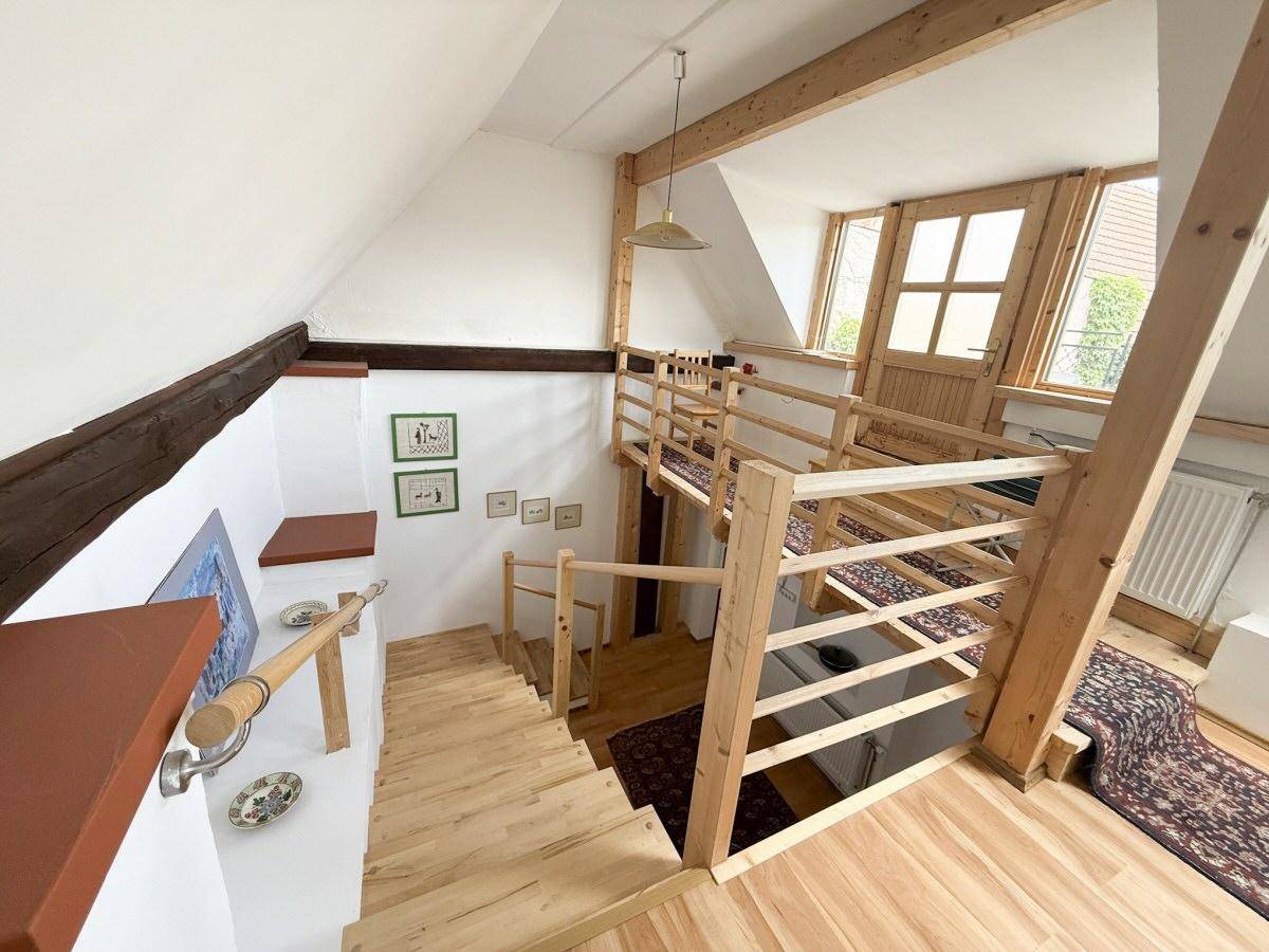 Heller Treppenaufgang im Dachgeschoss mit Holzstufen, Geländer und sichtbaren Holzbalken.