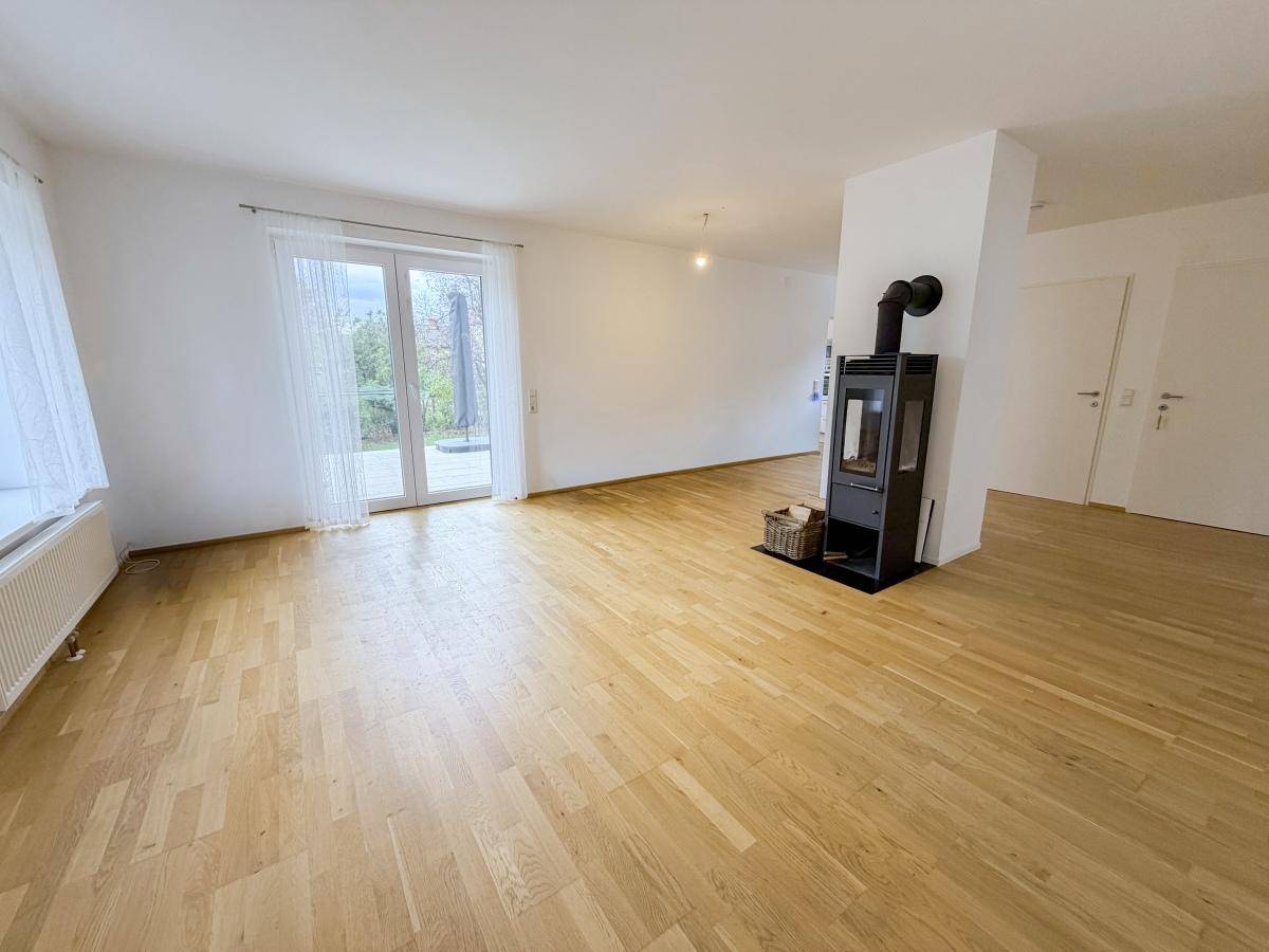 Helles Wohnzimmer mit Holzboden, Kaminofen und Zugang zur Terrasse.