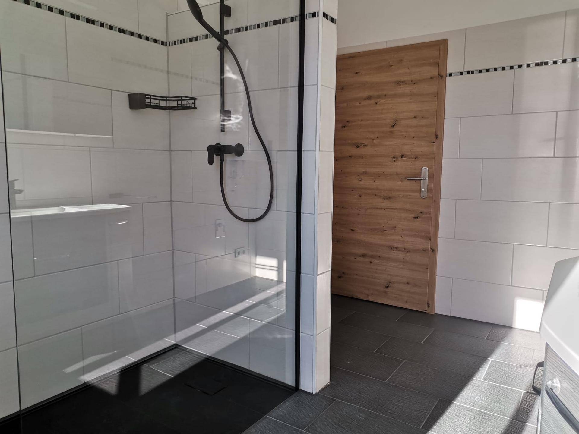 Modernes Badezimmer mit ebenerdiger Dusche, weißen Fliesen und dunklem Boden.