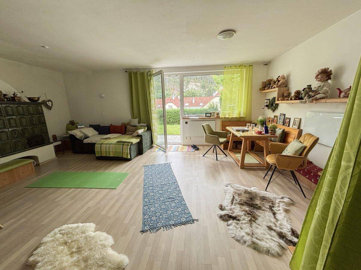 Helles Wohnzimmer mit traditionellem Kachelofen, gemütlicher Sitzecke und Zugang zum Garten.