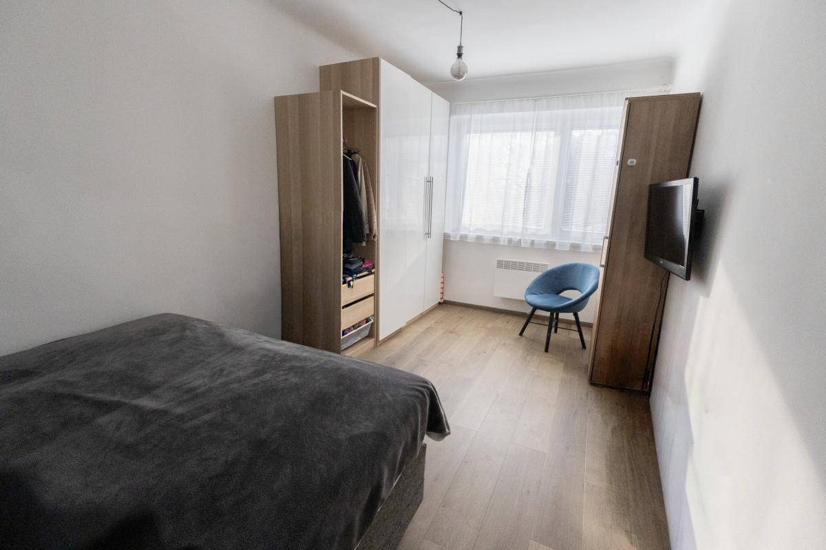 Gemütliches Schlafzimmer mit großem Fenster, Kleiderschrank und Holzboden.
