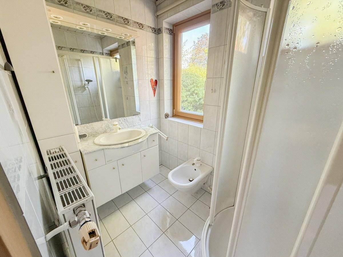 Helles Badezimmer mit Dusche, Bidet und Fenster, ausgestattet mit weißen Fliesen und Marmorwaschtisch.