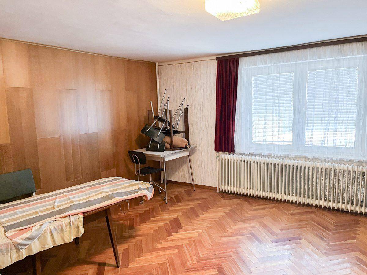 Geräumiges Zimmer mit Holzvertäfelung, Fischgrätparkett und großem Fenster.