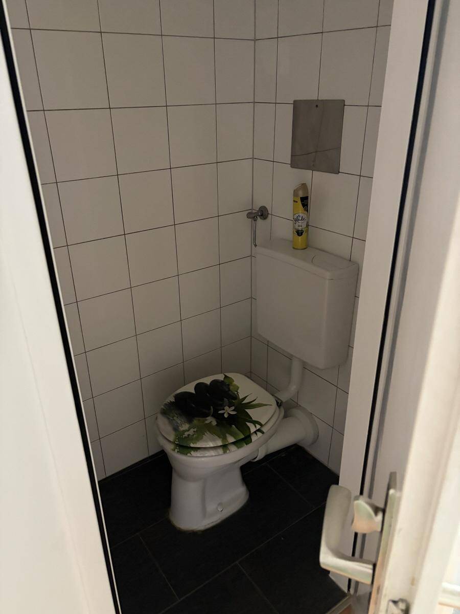 Kleines WC mit weiß gefliesten Wänden und dunklem Boden, funktional und sauber.
