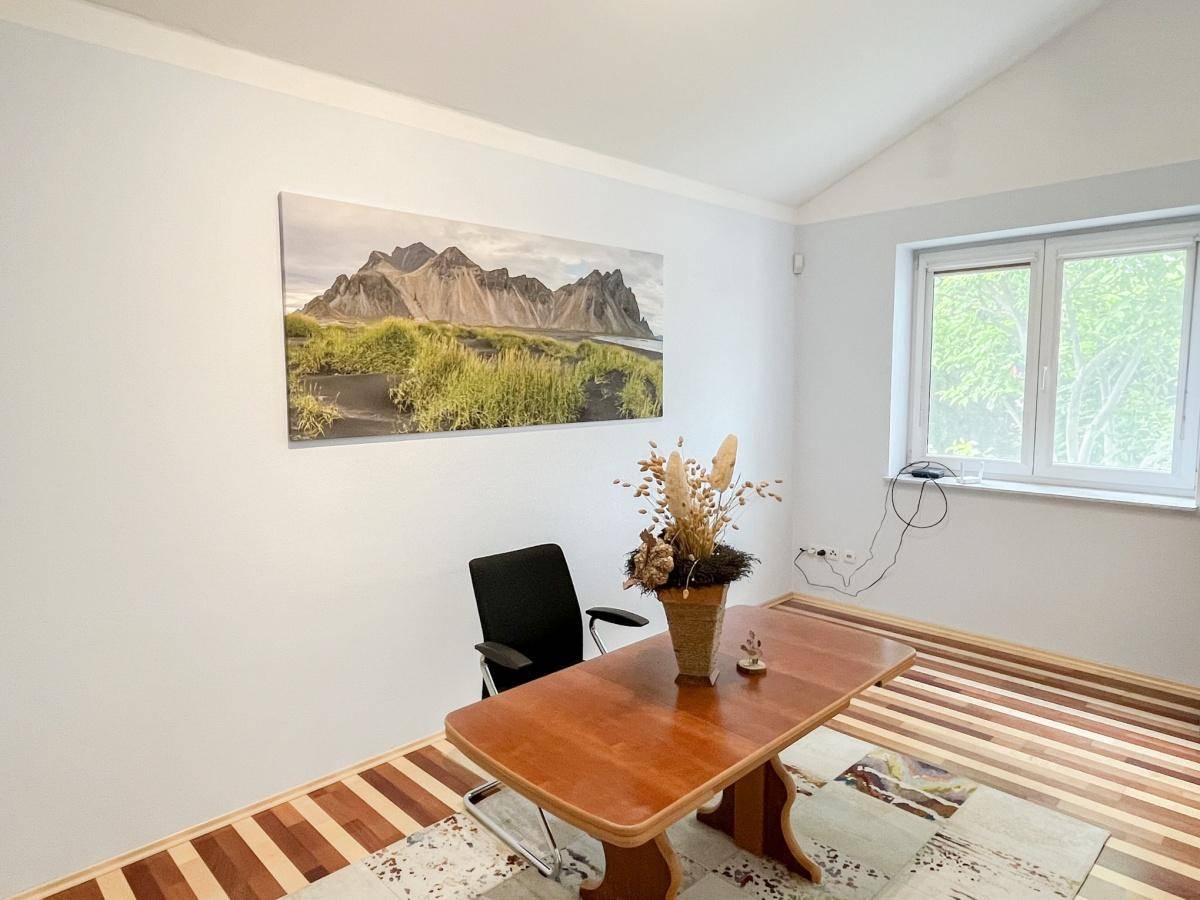 Helles Arbeitszimmer mit Schreibtisch, Fenster und einem inspirierenden Bergbild an der Wand.