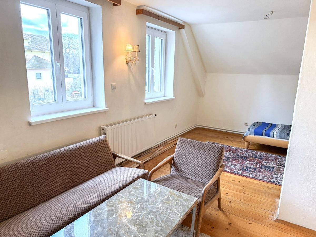 Gemütliches Zimmer mit Holzboden, Sitzgelegenheiten und Blick aus den Fenstern.