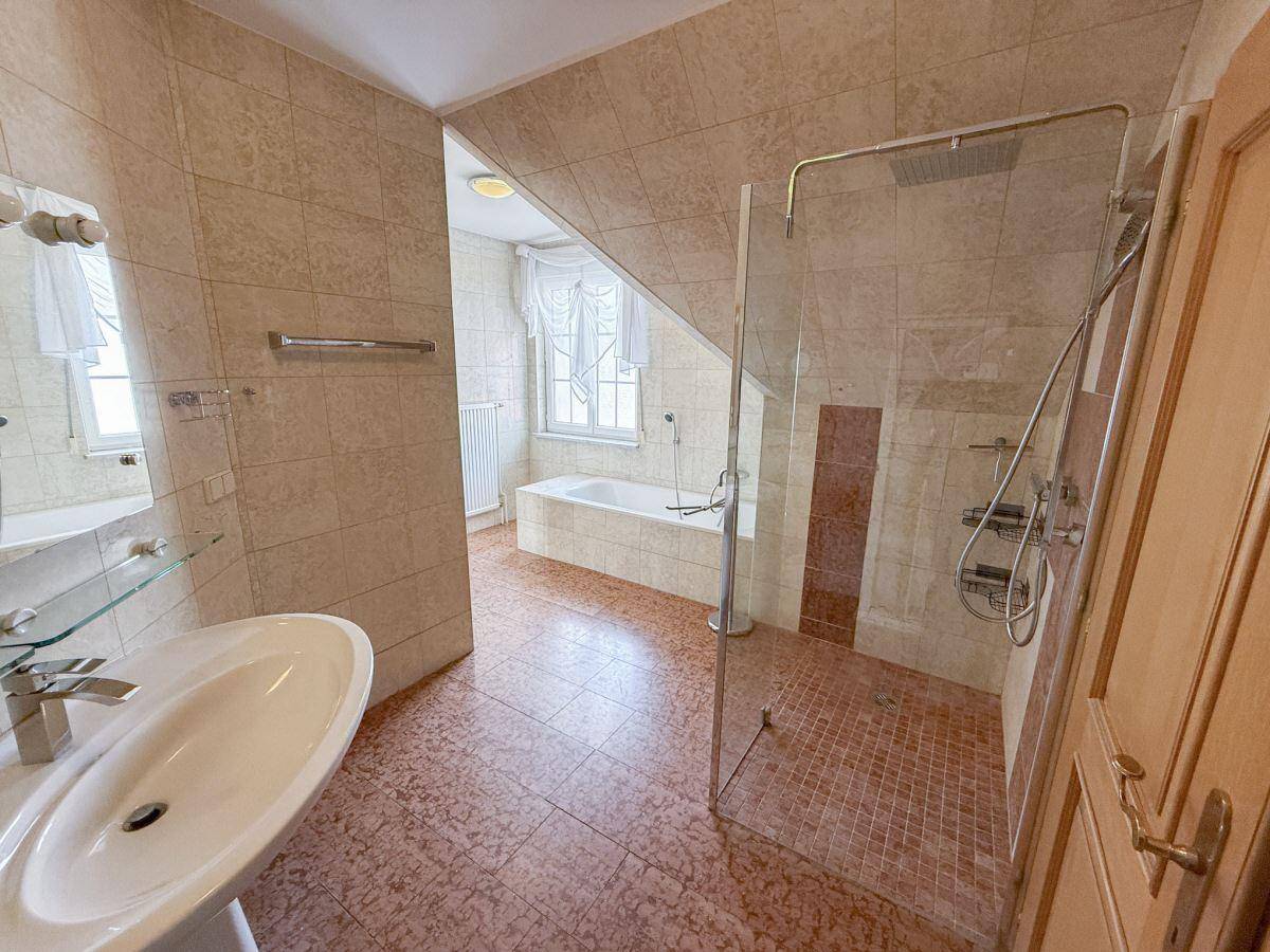 Badezimmer im Dachgeschoss mit Badewanne, Dusche und hellen Fliesen unter einer Dachschräge.