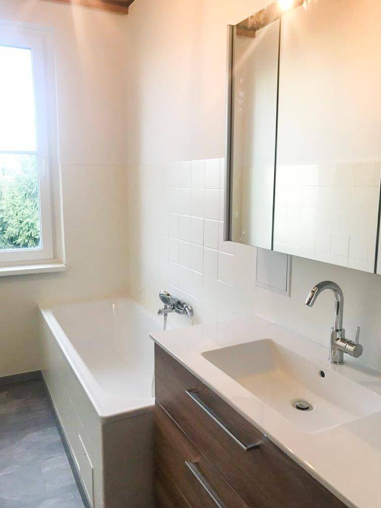 Ein helles Badezimmer mit Badewanne, Einzelwaschbecken und Spiegelschrank, ausgestattet mit einem Fenster.