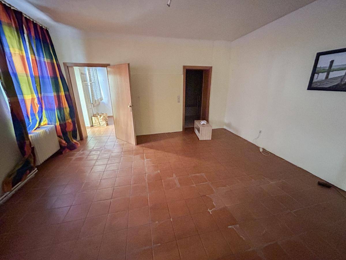 Geräumiger Raum mit Terrakotta-Fliesenboden und bunten Vorhängen an einem Fenster.