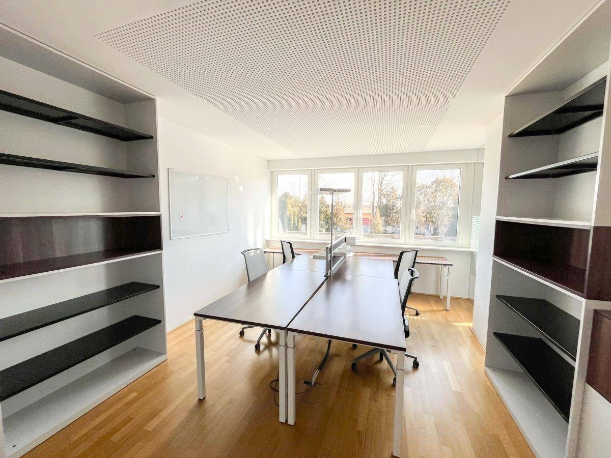 Großes, helles Büro mit mehreren Arbeitsplätzen, Holzfußboden und großen Fenstern, ideal für Teams.