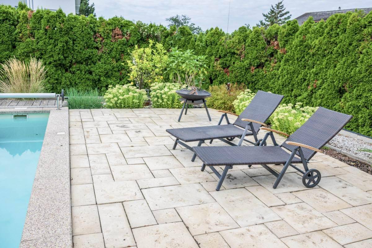 Poolbereich mit gepflasterter Terrasse, Sonnenliegen und Grill.