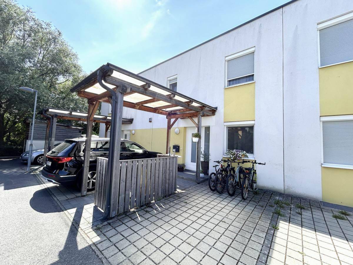 Vorderansicht des Reihenhauses mit Carport und gepflastertem Stellplatz für Fahrzeuge.