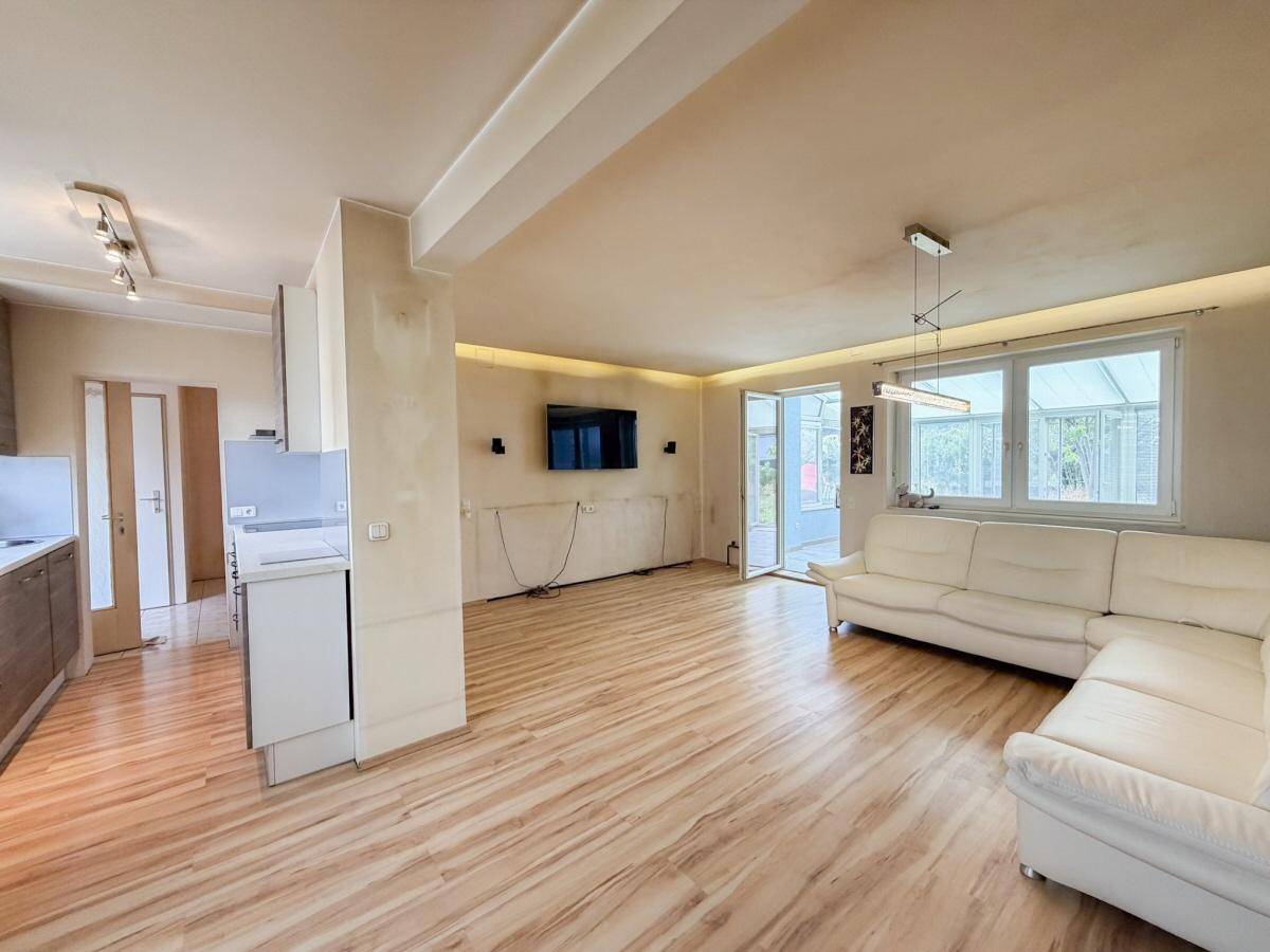 Offener Wohnbereich mit Laminatboden, weißem Sofa und Zugang zum Wintergarten.