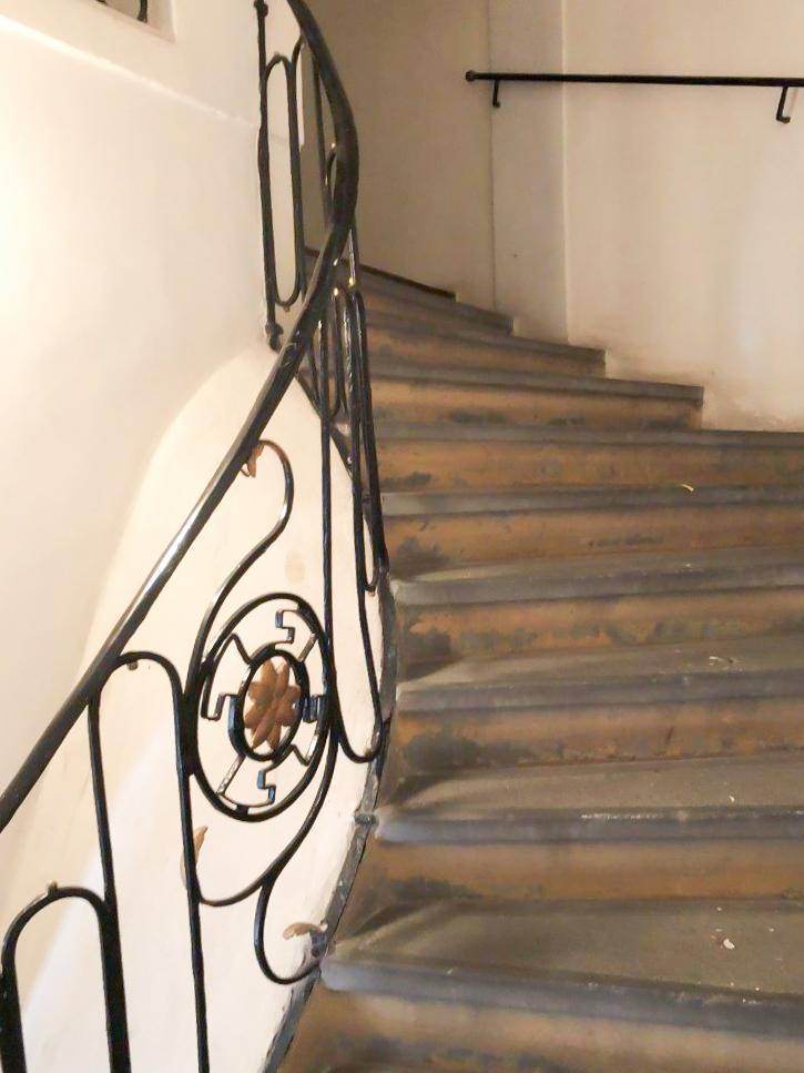 Historisches Treppenhaus mit einem kunstvollen schmiedeeisernen Geländer und abgenutzten Steinstufen.