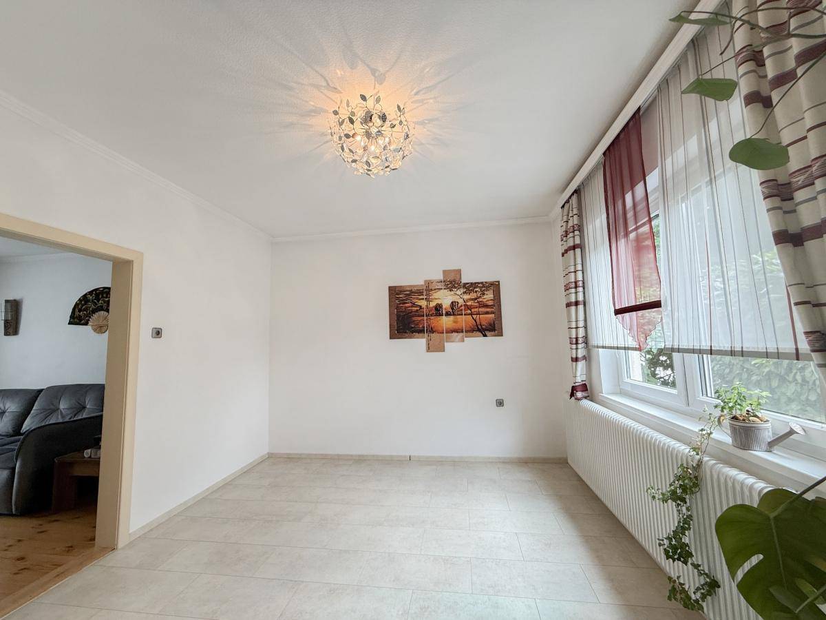 Heller Raum mit Fliesenboden und großem Fenster, bietet vielseitige Nutzungsmöglichkeiten als Ess- oder Wohnbereich.
