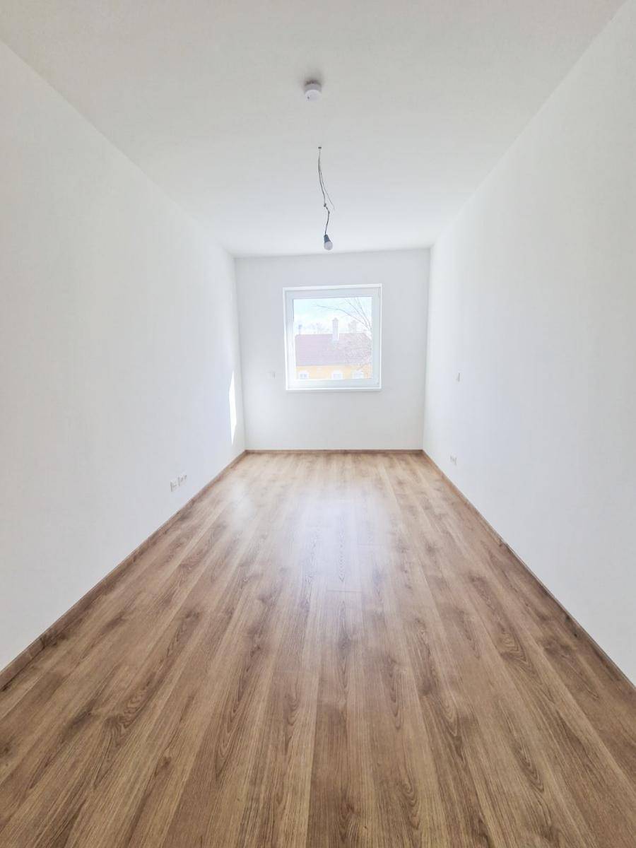 Langes, schmales Zimmer mit Laminatboden und einem Fenster am Ende, hell und unmöbliert.