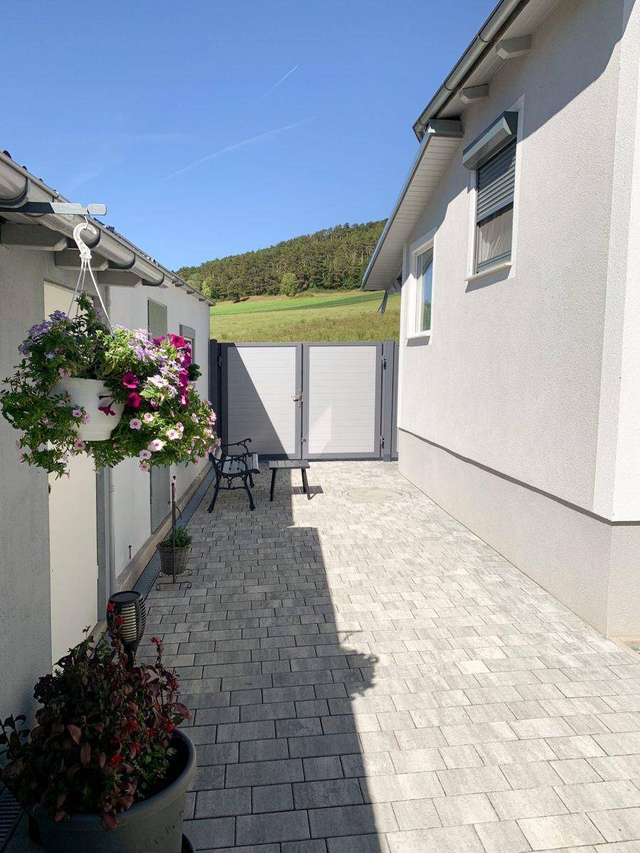 Gepflasterter Zugangsbereich zwischen den Gebäuden mit Blumenampel und Sitzbank.