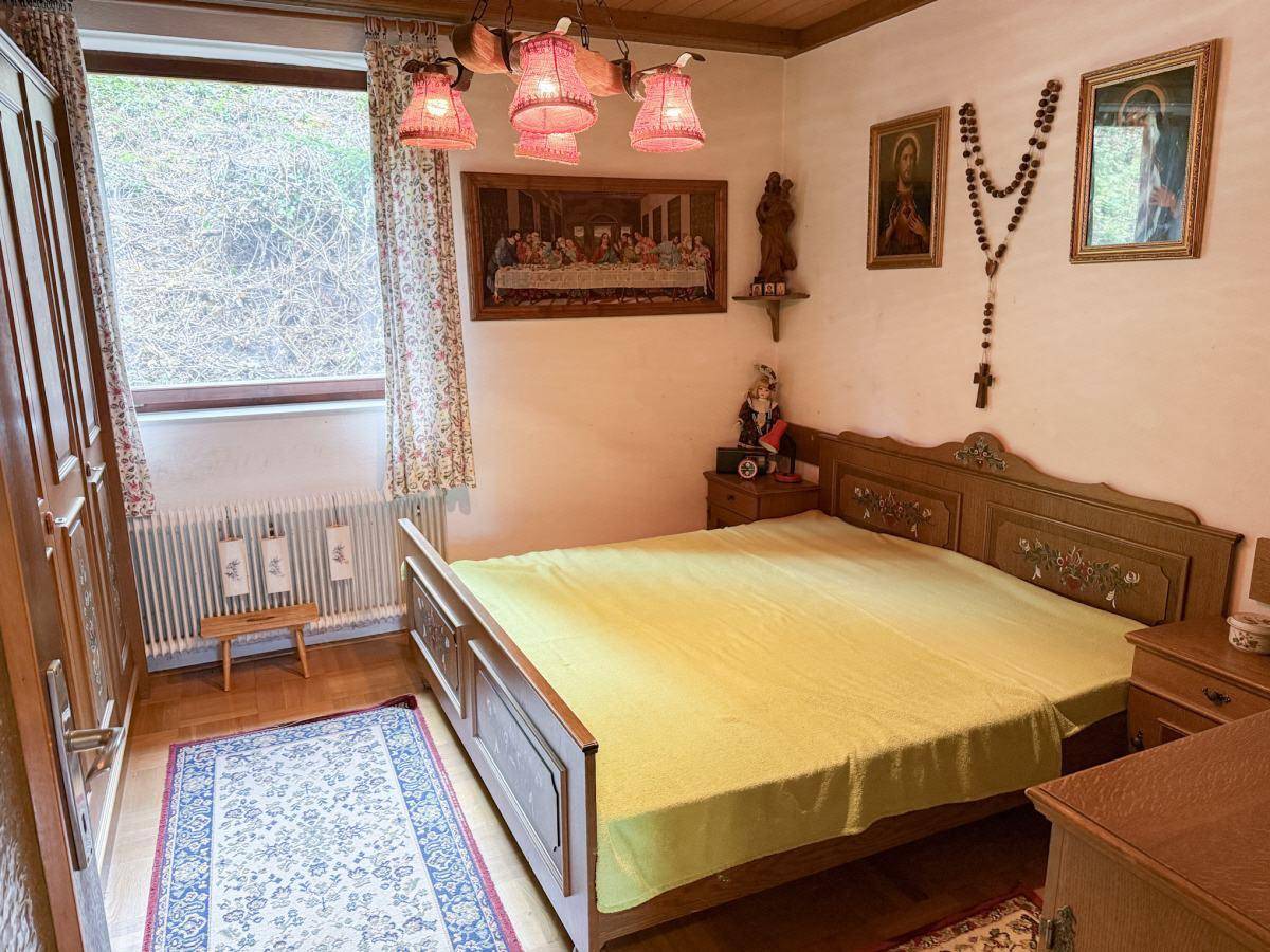 Schlafzimmer im traditionellen Stil mit Holzbett, Schrank und religiöser Dekoration.