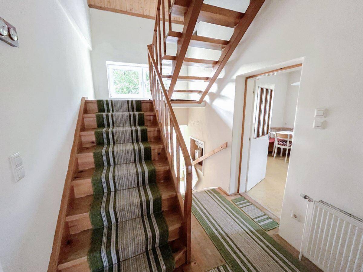 Holztreppe mit grün-weißem Teppichläufer, die die verschiedenen Etagen des Hauses verbindet.