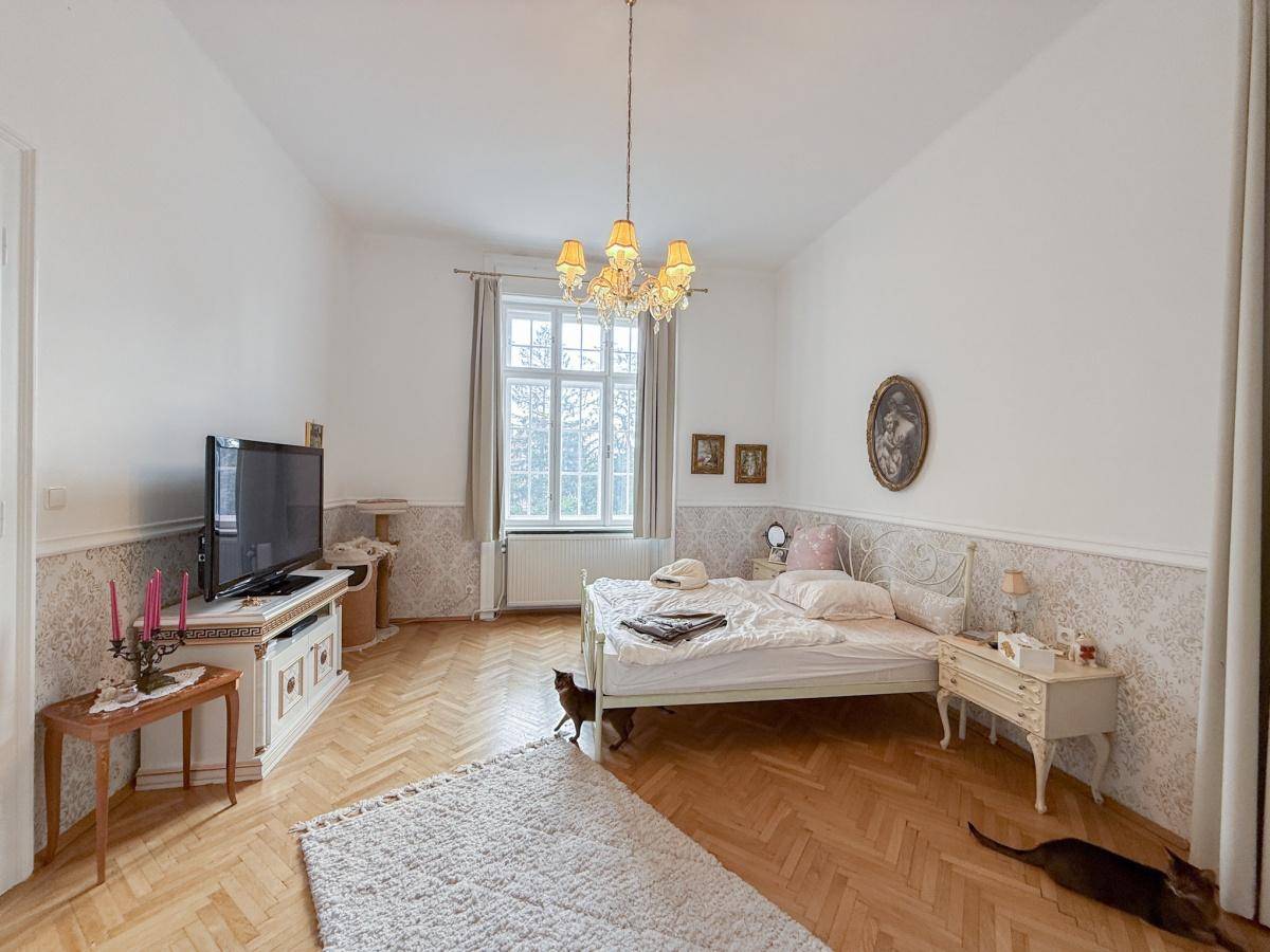 Gemütliches Schlafzimmer mit Fischgrätparkett, dekorativer Tapete und einem großen Fenster.
