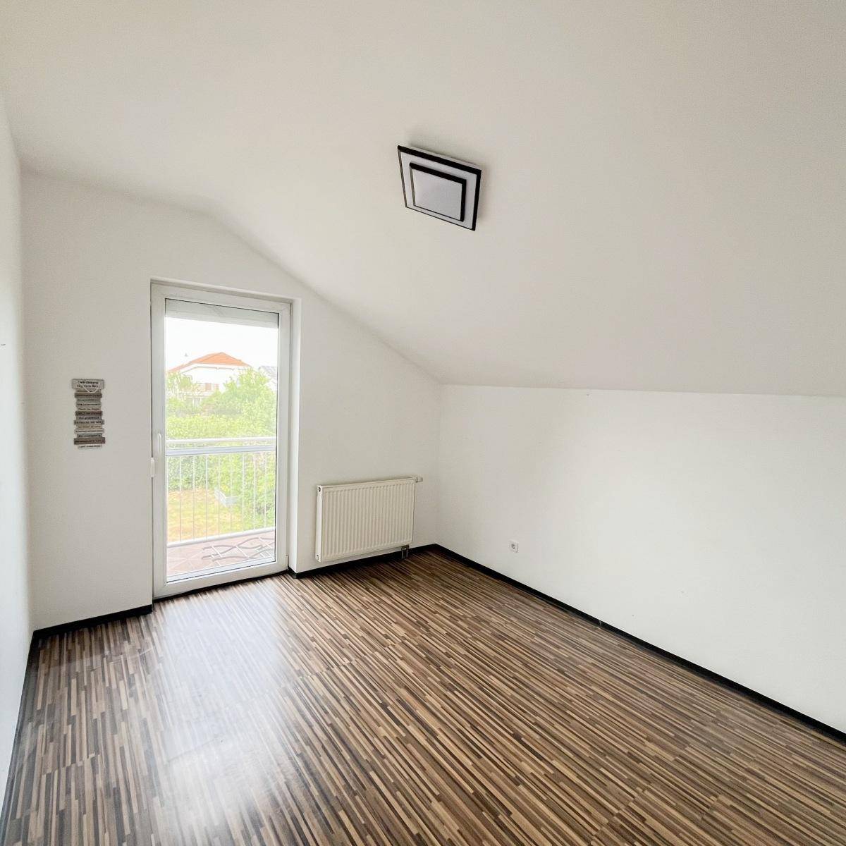 Helles Dachzimmer mit Laminatboden und Balkonzugang, ideal als Schlaf- oder Arbeitszimmer.