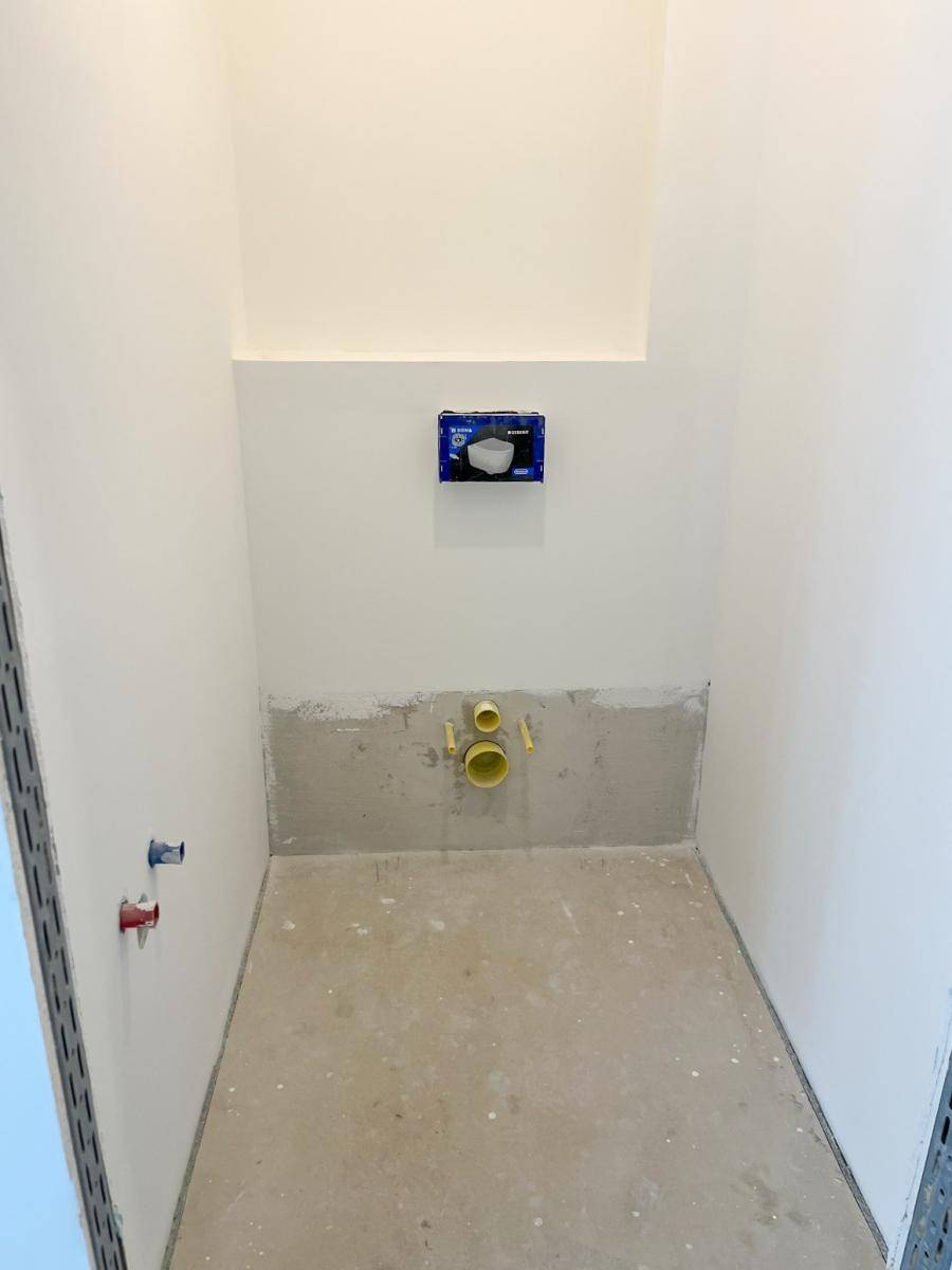Kleiner, unfertiger WC-Raum mit vorbereiteten Anschlüssen für die Toilette.