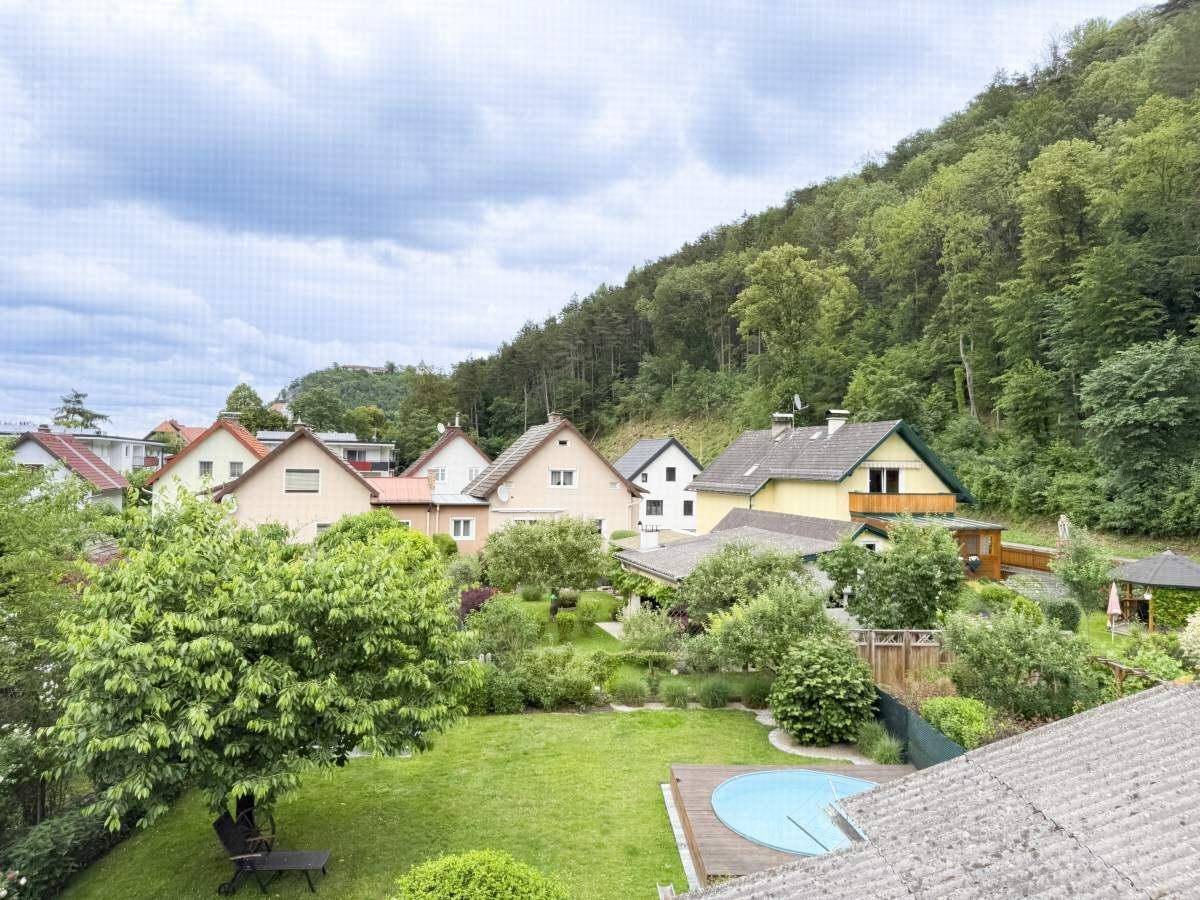Panoramablick über die Nachbarschaft mit Gärten, Häusern und bewaldeten Hügeln im Hintergrund.