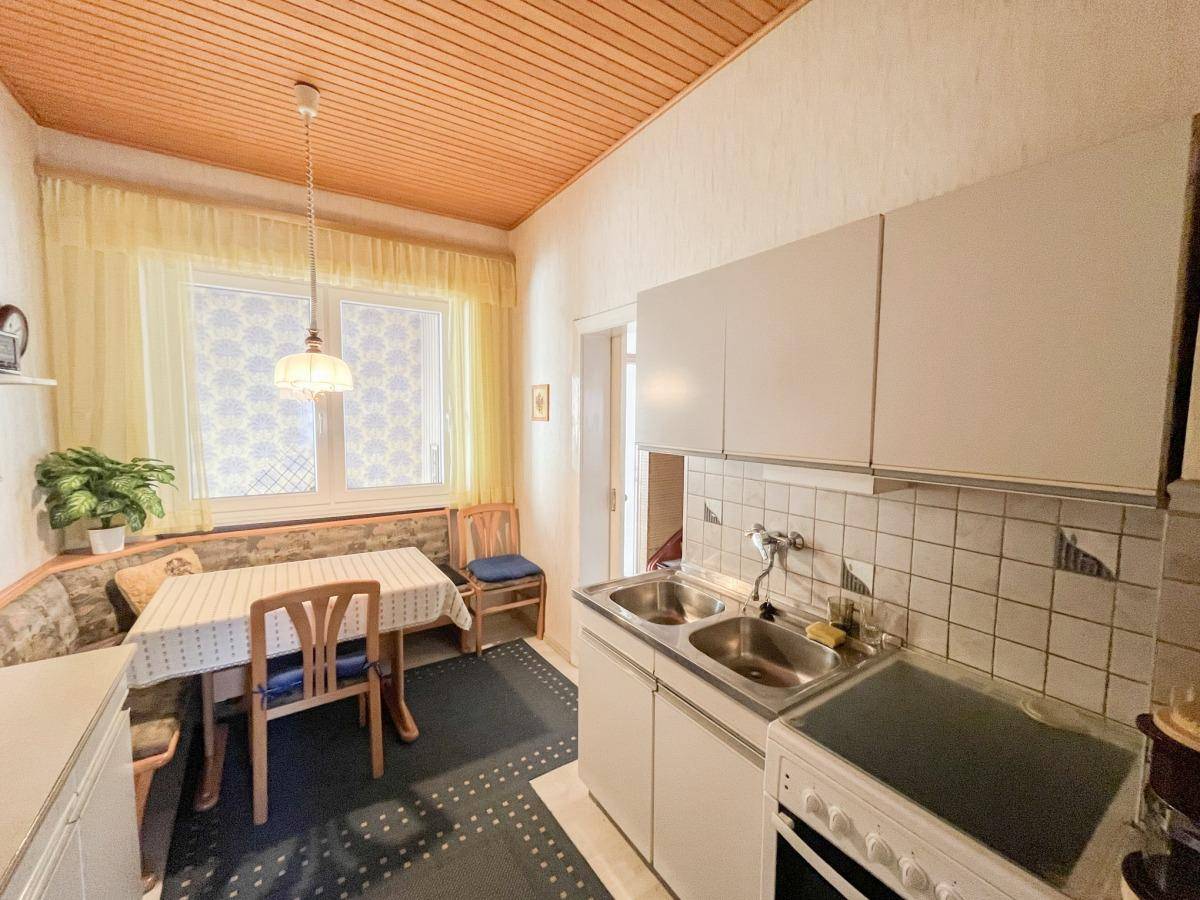 Kleine Küche mit Essbereich, weißen Schränken, Fliesenrückwand und Holzdecke.