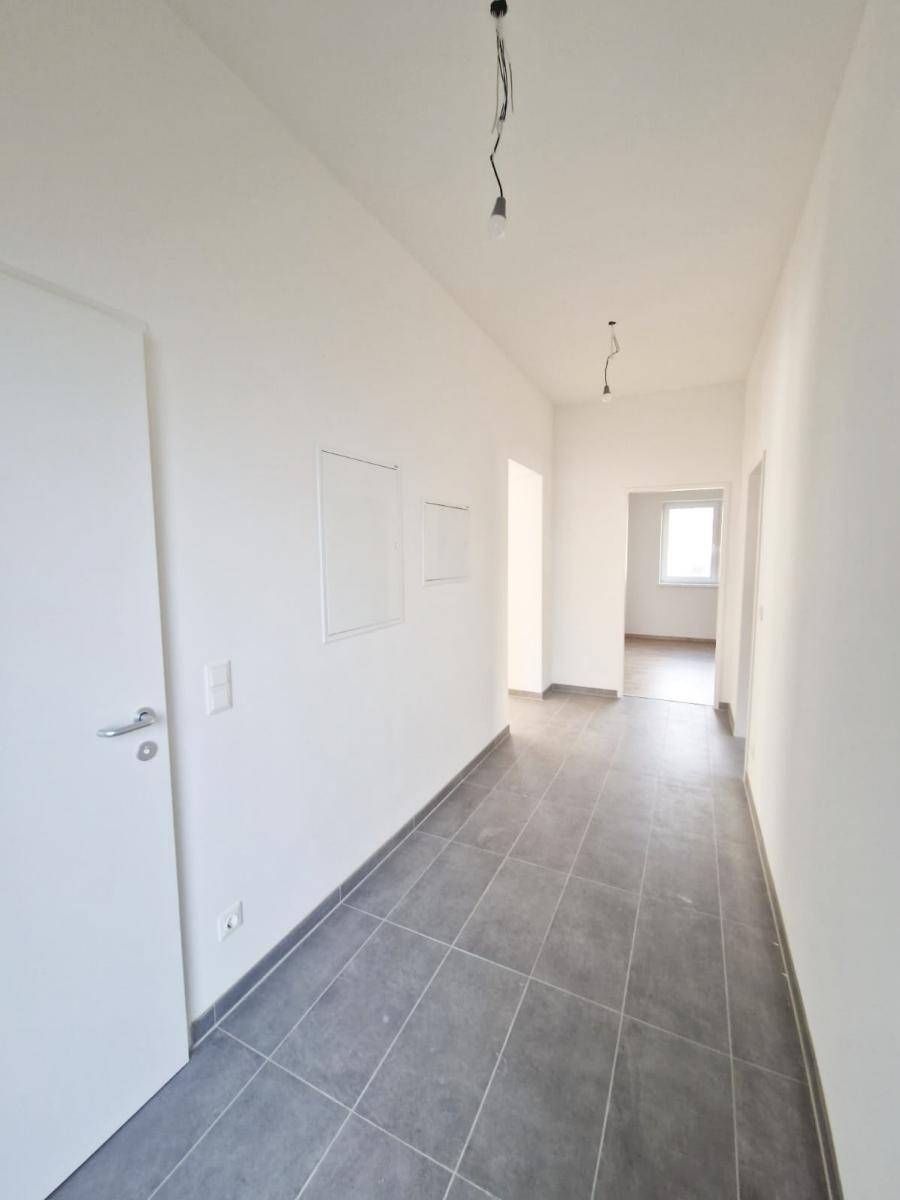 Langer, heller Flur mit modernen grauen Fliesen und weißen Wänden.