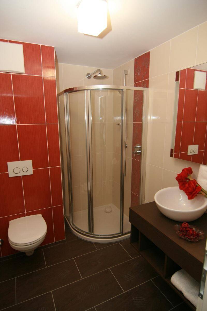 Modernes Badezimmer mit rotem Fliesenakzent, Duschkabine und wandhängendem WC.