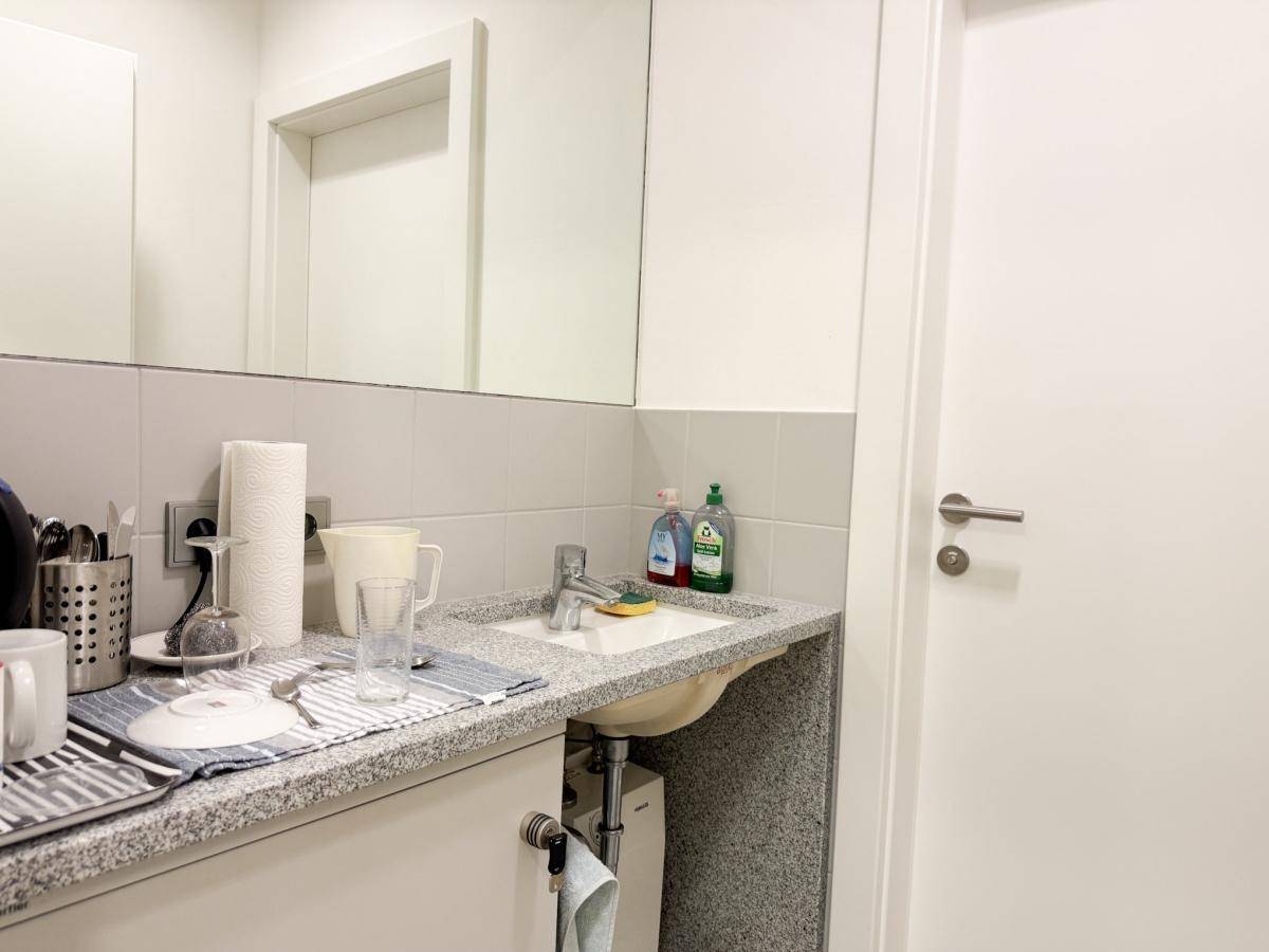 Kleine Küchenzeile mit Spülbecken, Granit-Arbeitsplatte und Geschirr.
