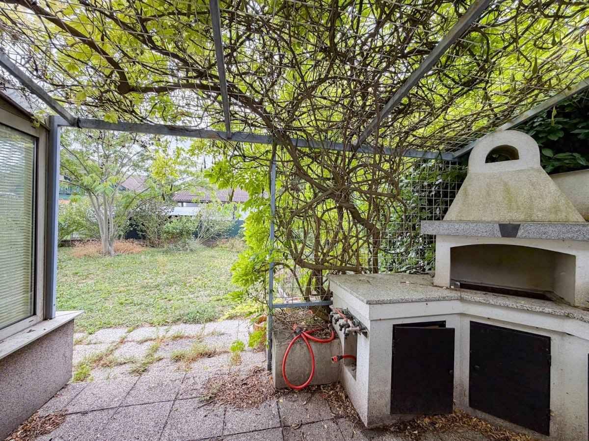 Überdachter Außenbereich mit gemauertem Grill und Sitzgelegenheit im Garten.
