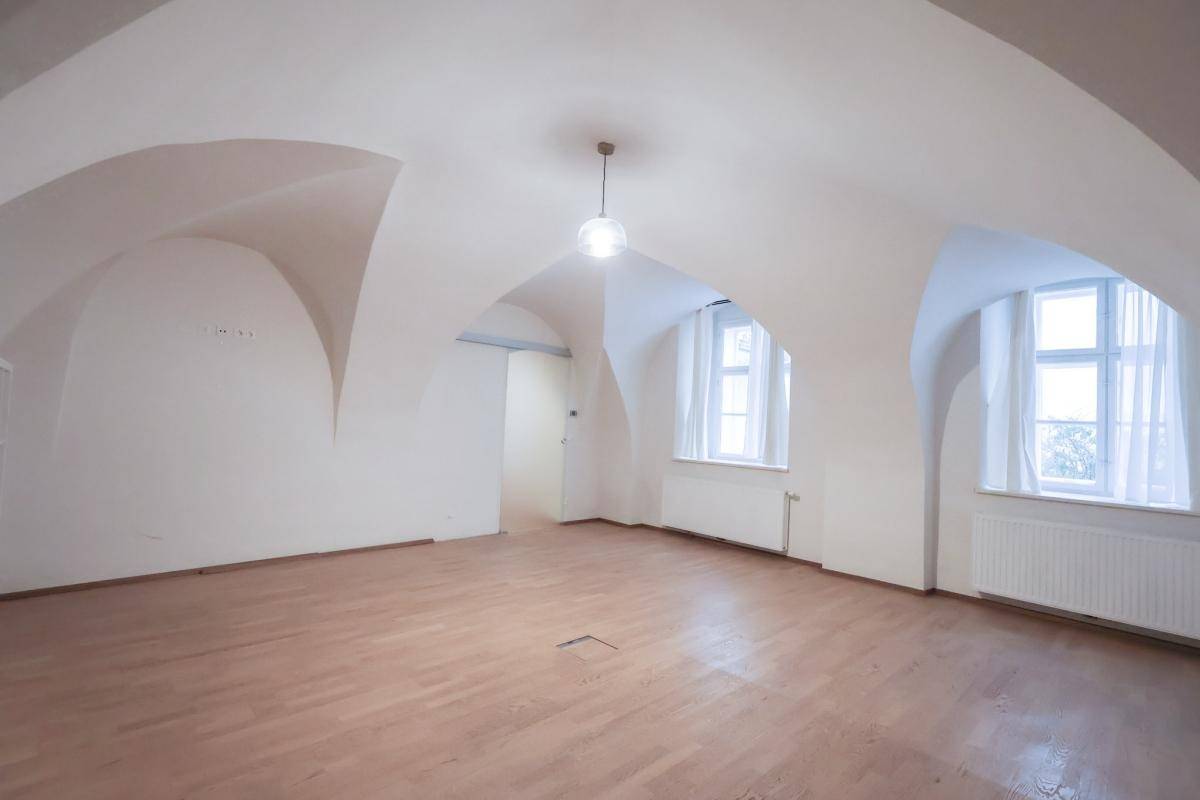 Heller Raum mit gewölbter Decke, Holzboden und zwei Fenstern, die viel Licht spenden.