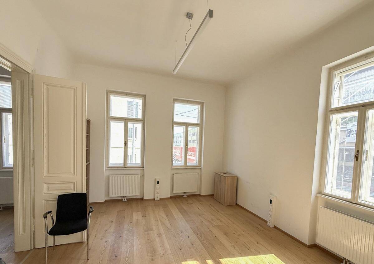 Geräumiger Büroraum mit hellen Wänden, Holzparkett und großen Fenstern für viel Tageslicht.