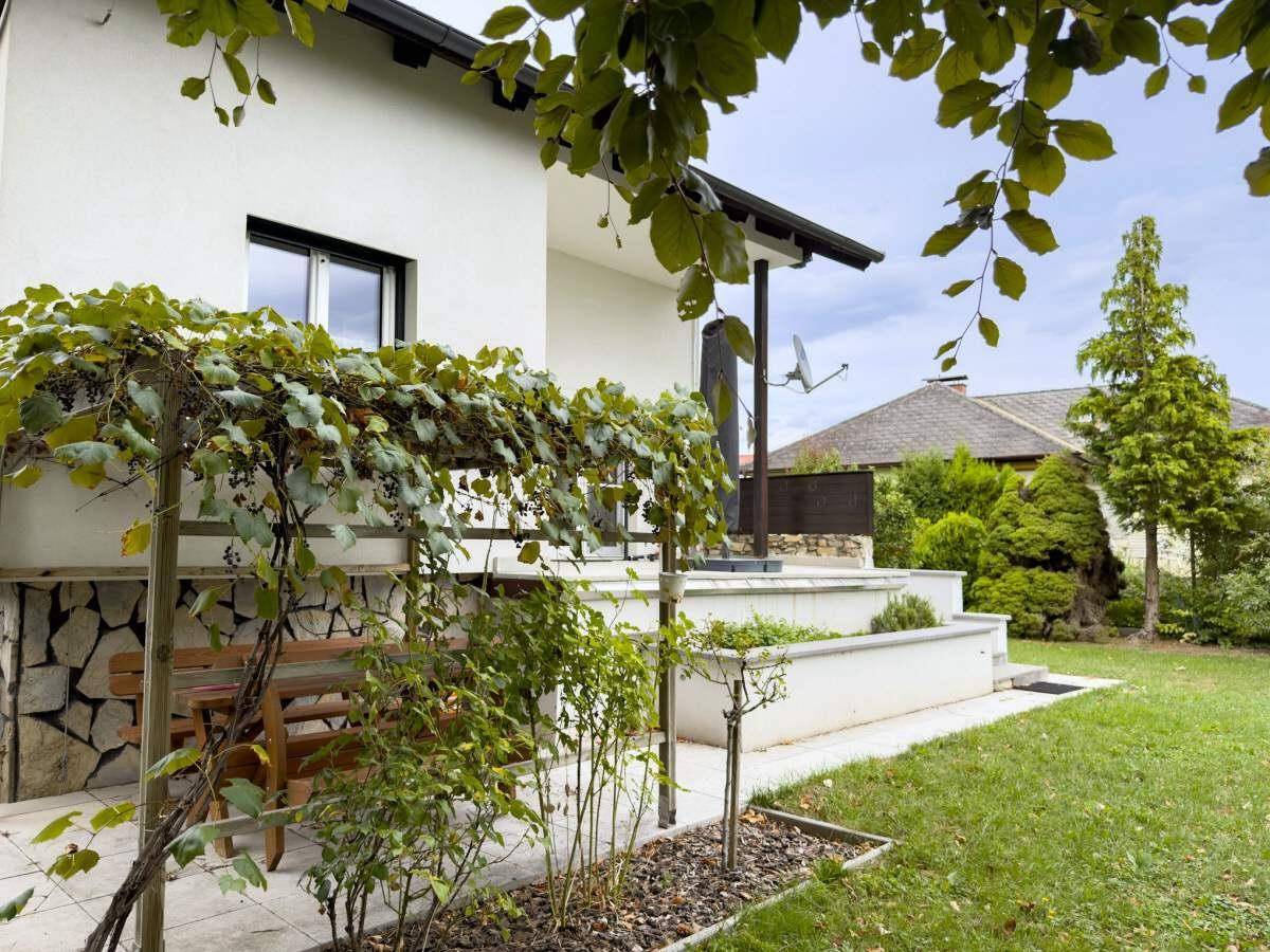 Gemütlicher Gartenbereich mit Sitzgelegenheit unter Weinreben und Blick auf das Haus.