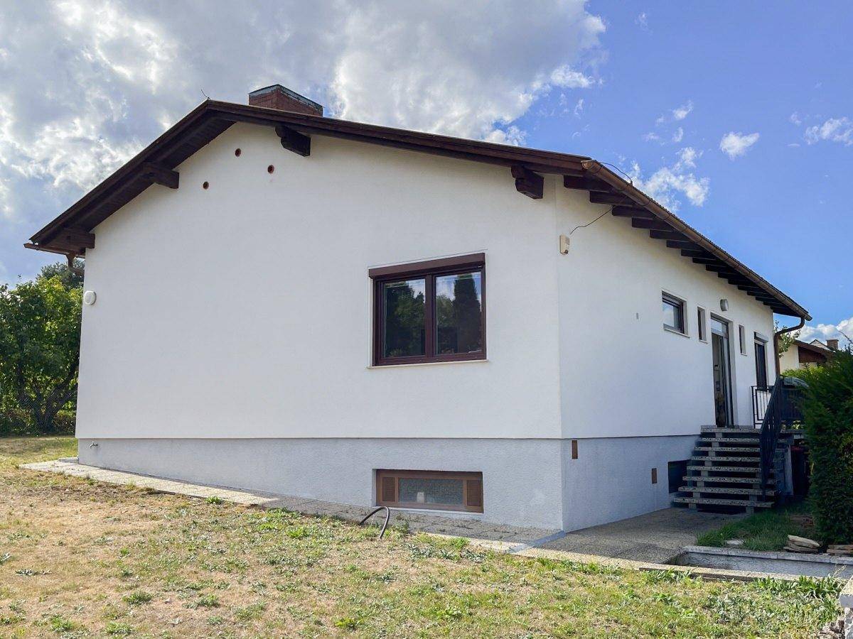 Seitenansicht des Hauses mit weißer Fassade, braunen Fenstern und Satteldach.