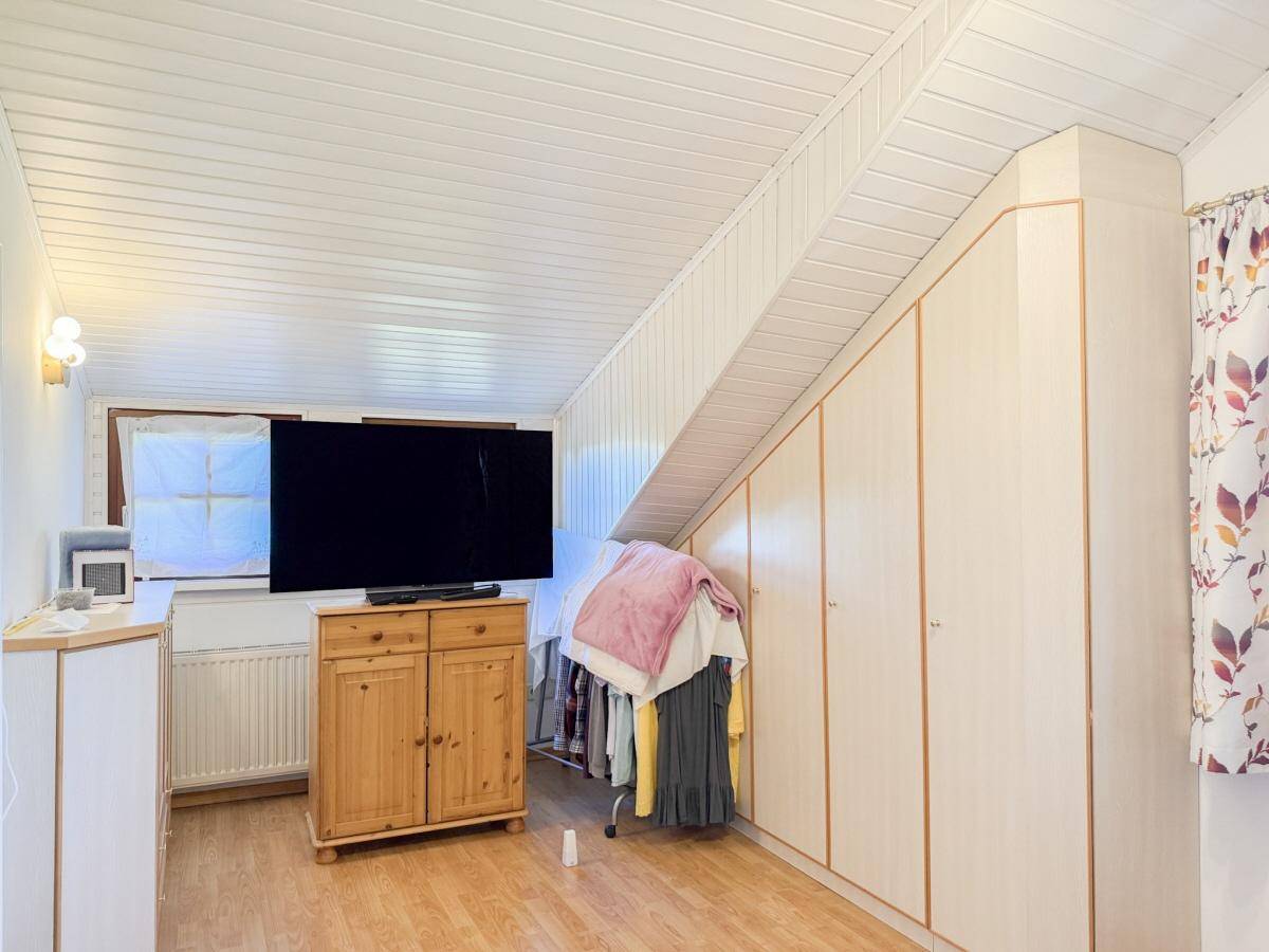 Dachgeschoss-Schlafzimmer mit schräger Decke, Holzpaneelen und praktischen Einbauschränken.
