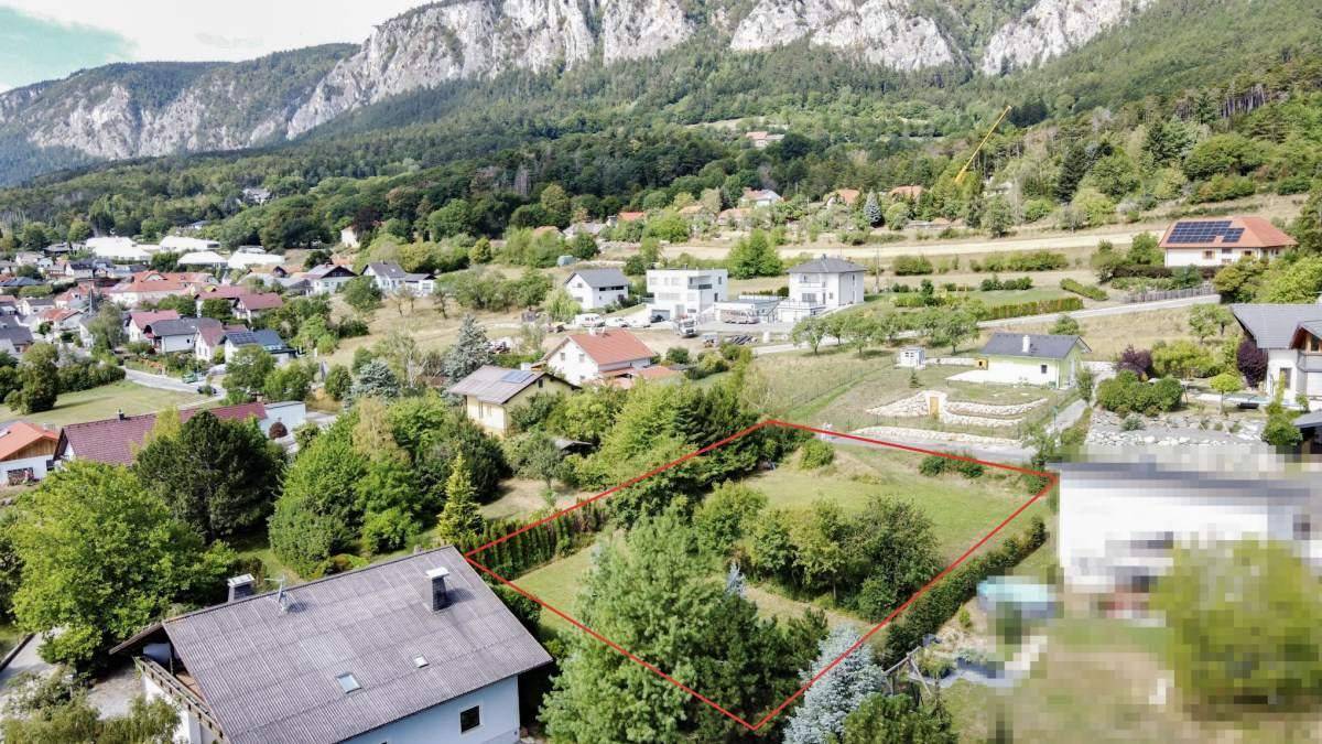 Luftaufnahme eines Baugrundstücks mit Bergblick, umgeben von Wohnbebauung und viel Grün.