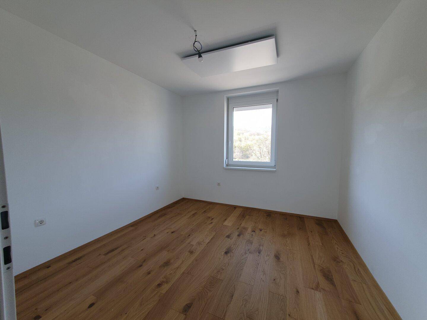 Helles Schlafzimmer mit Holzboden und einem Fenster, das viel Tageslicht hereinlässt.