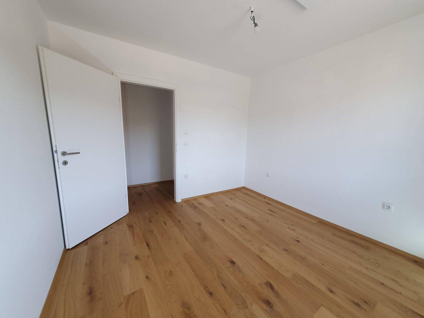 Leeres Zimmer mit Holzboden und weiß gestrichenen Wänden, bereit zur individuellen Gestaltung.