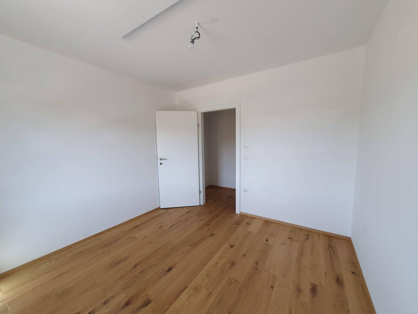 Unmöbliertes Zimmer mit Holzboden und weiß gestrichenen Wänden, ideal als Schlaf- oder Arbeitszimmer.