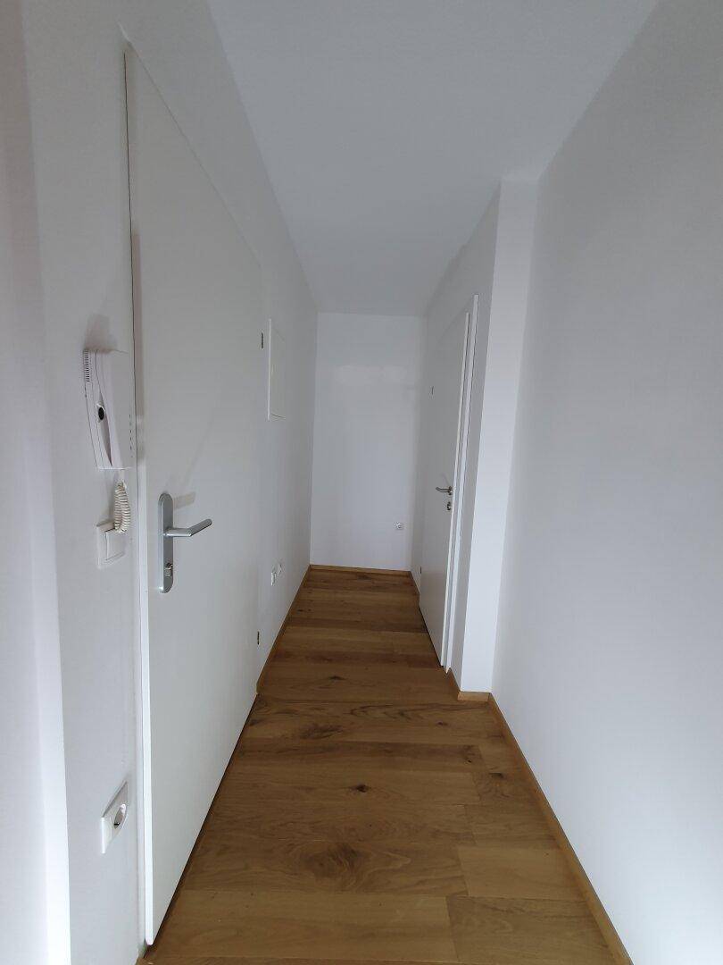 Langer, heller Flur mit Holzboden und weißen Wänden, der zu weiteren Räumen führt.