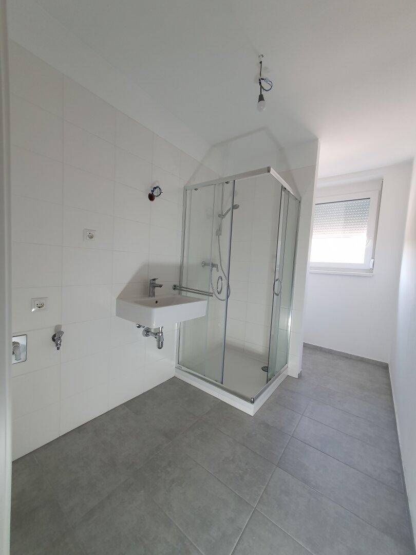 Modernes Badezimmer mit Duschkabine, Waschbecken und grauen Bodenfliesen.
