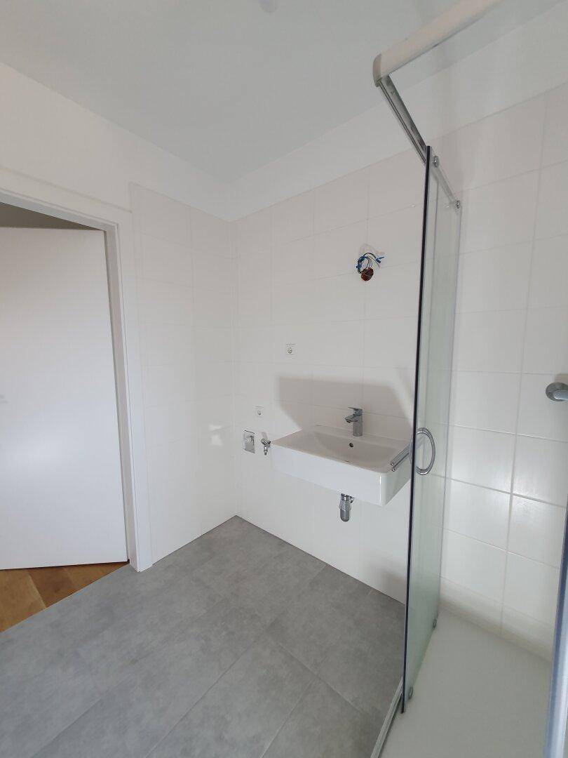 Helles Badezimmer mit Duschkabine und modernem Waschbecken, ausgestattet mit weißen Fliesen.