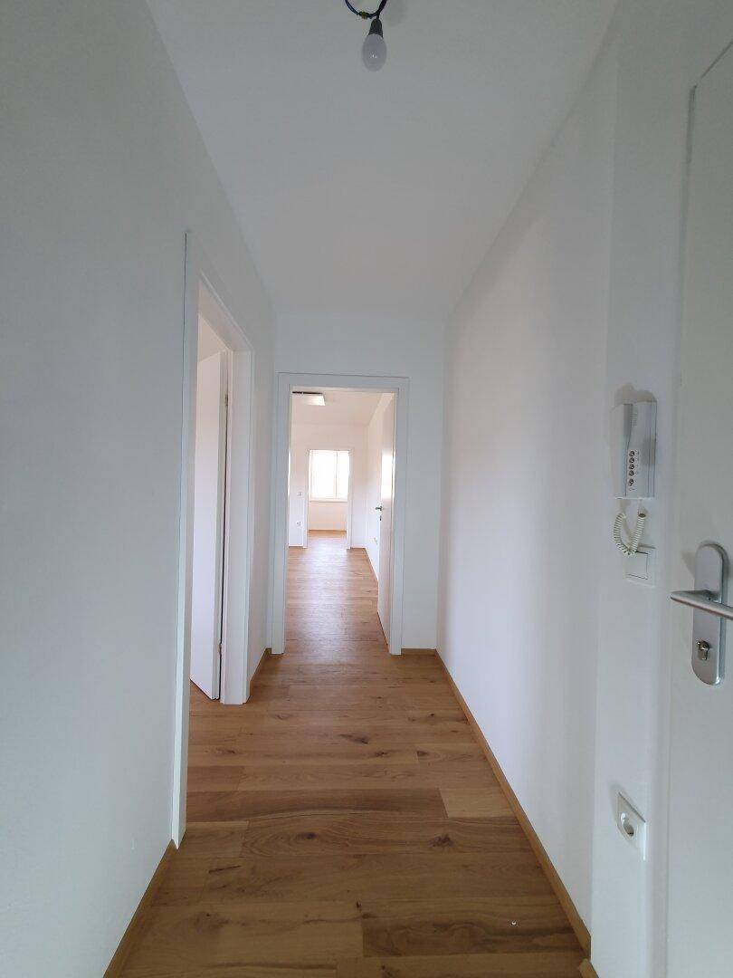 Heller Flur mit Holzboden und weißen Wänden, der einen Blick in die angrenzenden Zimmer bietet.