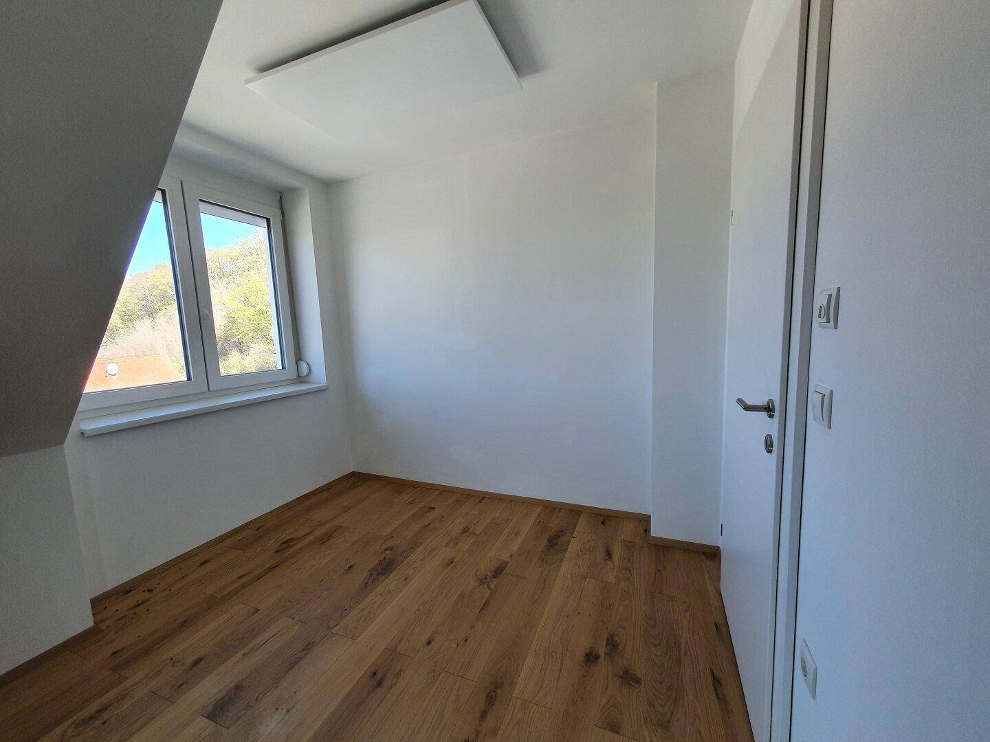 Modernes Dachzimmer mit Holzboden, weiß gestrichenen Wänden und einem großen Fenster.
