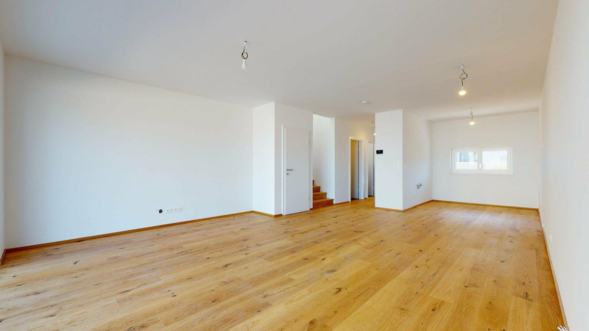 Geräumiger, heller Wohnbereich mit neuem Holzparkett und Zugang zu weiteren Räumen.